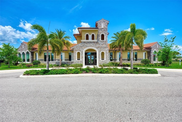 mediterranean / spanish house with stone siding, a tile roof, and stucco siding