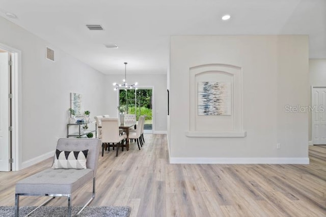 corridor with light wood-type flooring, a notable chandelier, baseboards, and visible vents