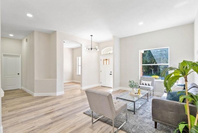 living area featuring a notable chandelier, arched walkways, baseboards, and light wood finished floors