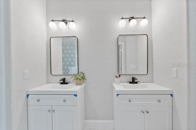 bathroom featuring baseboards, a sink, and two vanities