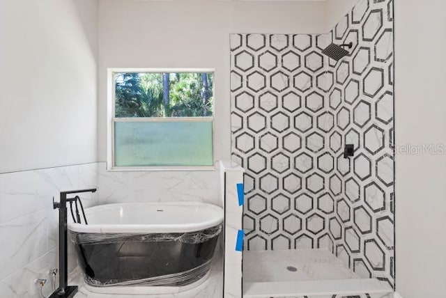 bathroom with tile walls, a wainscoted wall, tiled shower, and a freestanding bath