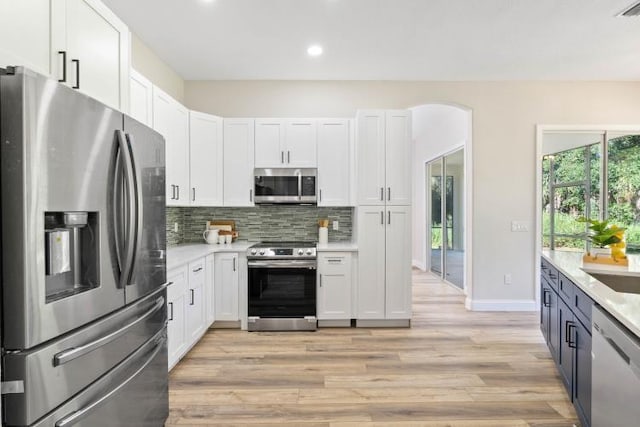 kitchen with light countertops, backsplash, appliances with stainless steel finishes, light wood-style flooring, and white cabinets