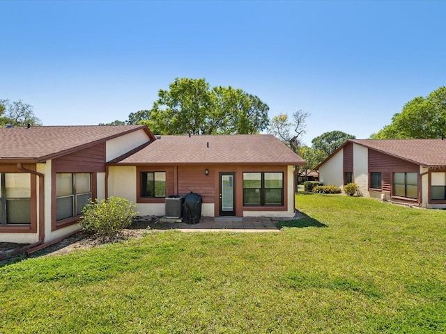 back of property with central AC unit, a shingled roof, a patio area, and a yard