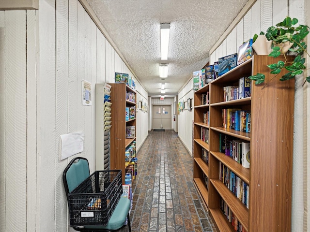 hallway featuring brick floor, wood walls, and a textured ceiling