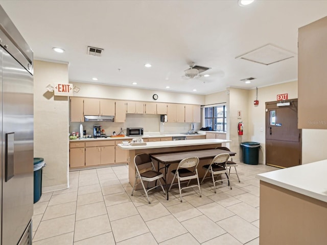 kitchen with light tile patterned flooring, light countertops, a breakfast bar, under cabinet range hood, and stainless steel built in fridge