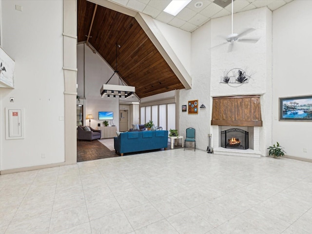 tiled living room with baseboards, a high ceiling, a drop ceiling, ceiling fan, and a brick fireplace