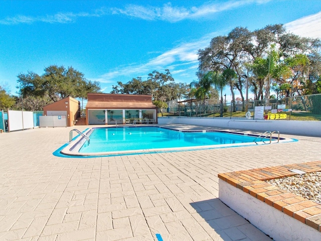 community pool with an outbuilding, a storage structure, fence, and a patio area