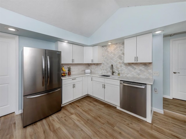 kitchen with appliances with stainless steel finishes, a sink, vaulted ceiling, light countertops, and white cabinets