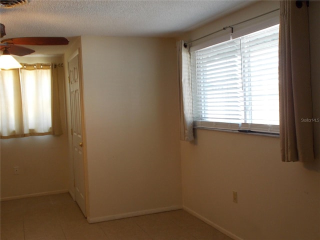 unfurnished room with a ceiling fan, light tile patterned floors, baseboards, and a textured ceiling