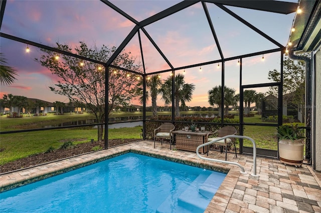 pool at dusk with a lawn, a water view, a lanai, and a patio area