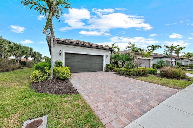 view of front of property featuring a tile roof, a front yard, stucco siding, an attached garage, and decorative driveway
