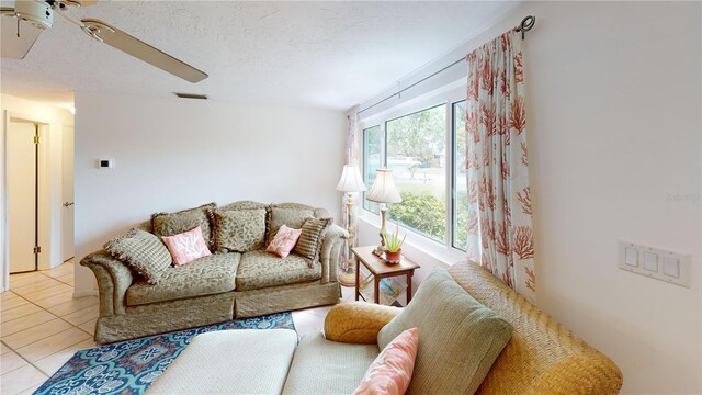 living room featuring light tile patterned flooring, a textured ceiling, visible vents, and ceiling fan