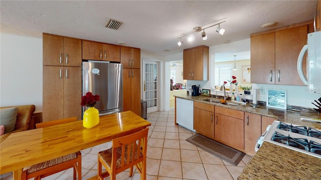 kitchen featuring visible vents, white appliances, a sink, brown cabinetry, and light tile patterned floors