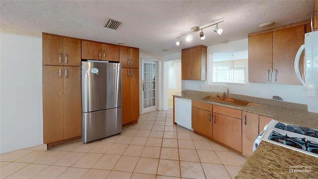 kitchen with a sink, brown cabinetry, light tile patterned floors, white appliances, and visible vents