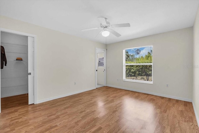 unfurnished bedroom featuring wood finished floors, ceiling fan, baseboards, and a spacious closet