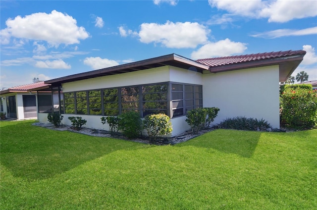 view of side of property with stucco siding, a tiled roof, and a yard