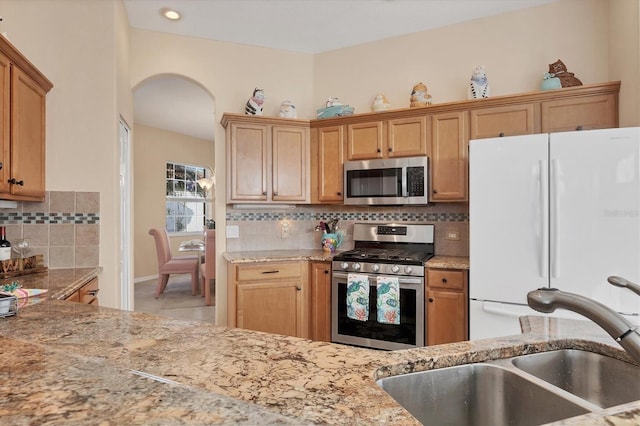 kitchen with a sink, light stone countertops, appliances with stainless steel finishes, arched walkways, and decorative backsplash