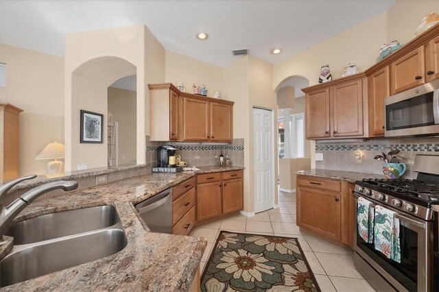 kitchen with light tile patterned floors, stainless steel appliances, a sink, arched walkways, and visible vents