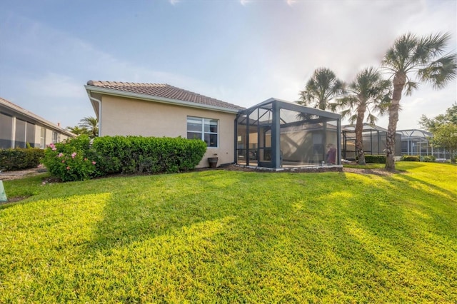rear view of property with a lawn, stucco siding, a lanai, and a tiled roof