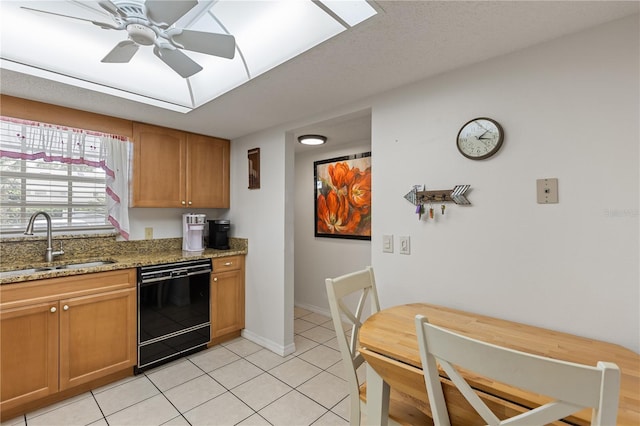 kitchen with light stone countertops, black dishwasher, a ceiling fan, a sink, and light tile patterned floors