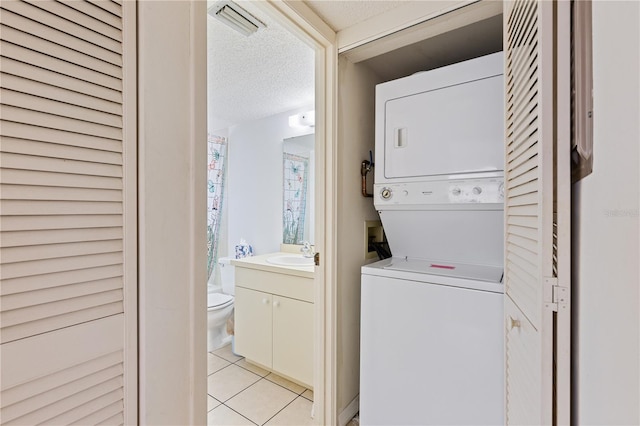 laundry area with a textured ceiling, stacked washer / dryer, laundry area, a sink, and light tile patterned floors