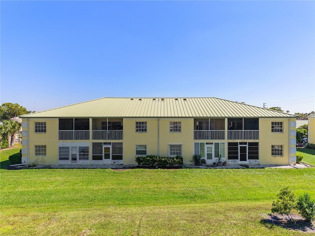 rear view of property featuring stucco siding, metal roof, a sunroom, and a yard