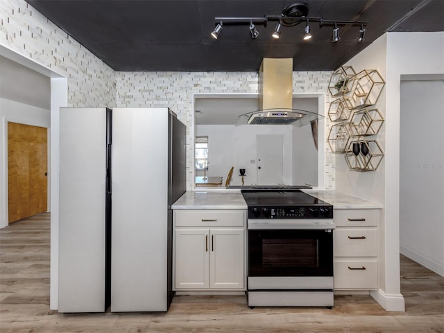 kitchen featuring light countertops, island range hood, range with electric stovetop, freestanding refrigerator, and light wood-style flooring