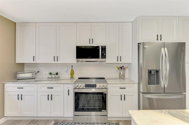 kitchen with appliances with stainless steel finishes, light stone counters, white cabinetry, a toaster, and backsplash
