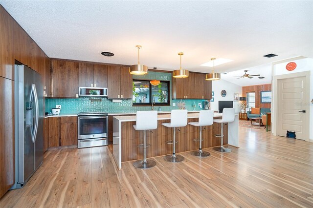23 Tiffany St, Englewood, FL 34223 - kitchen with stainless steel appliances, light countertops, decorative backsplash, brown cabinets, and light wood-type flooring