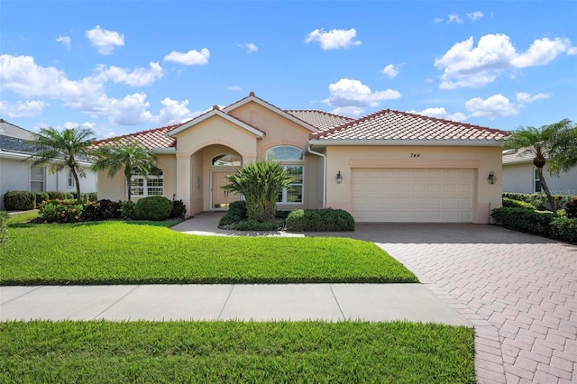 mediterranean / spanish-style house with stucco siding, a front lawn, an attached garage, and a tile roof