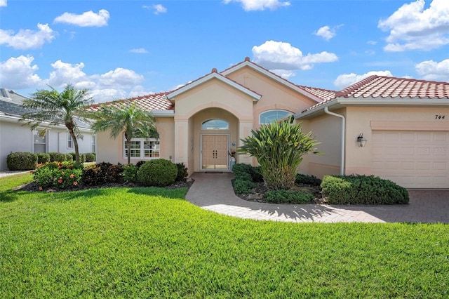 mediterranean / spanish-style house featuring an attached garage, stucco siding, a tiled roof, and a front lawn