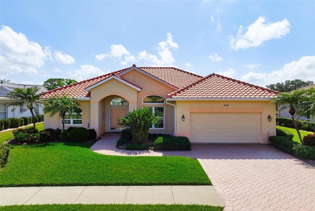 mediterranean / spanish home with stucco siding, driveway, a front yard, a garage, and a tiled roof