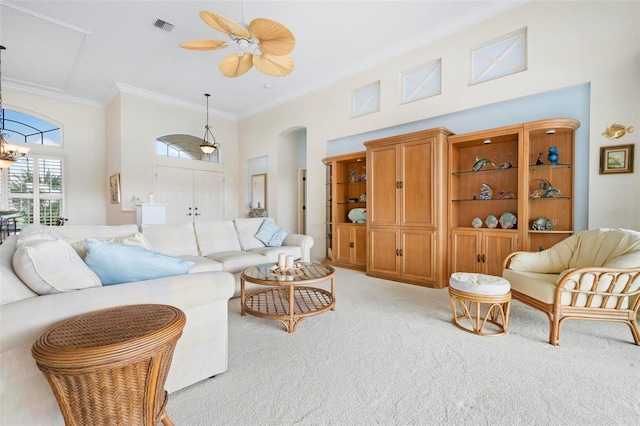 carpeted living room featuring visible vents, arched walkways, crown molding, a towering ceiling, and ceiling fan with notable chandelier