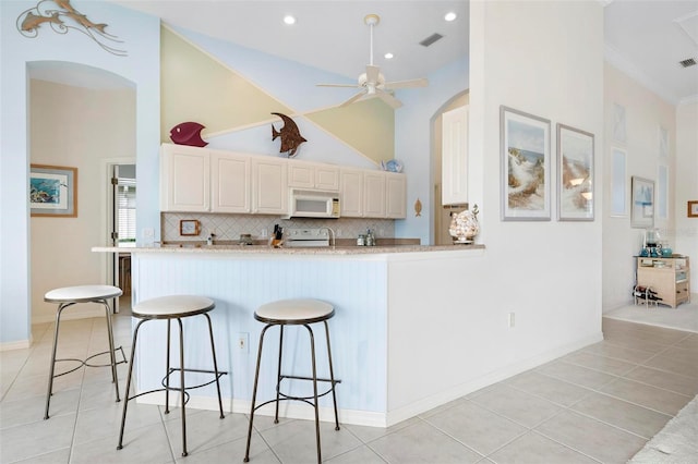kitchen featuring a kitchen breakfast bar, white appliances, a ceiling fan, light tile patterned flooring, and visible vents