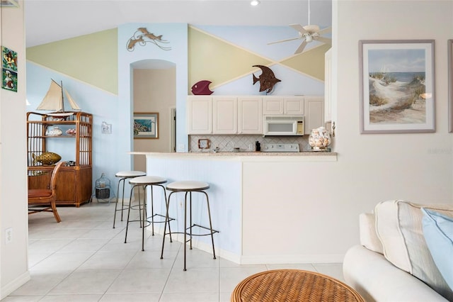 kitchen with light tile patterned floors, light countertops, white microwave, backsplash, and a breakfast bar area