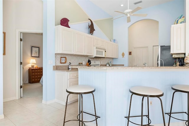 kitchen with tasteful backsplash, white microwave, ceiling fan, and a breakfast bar area