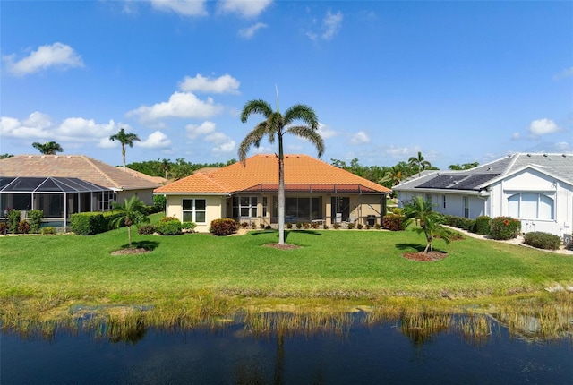rear view of property featuring a water view, a yard, stucco siding, and a tile roof