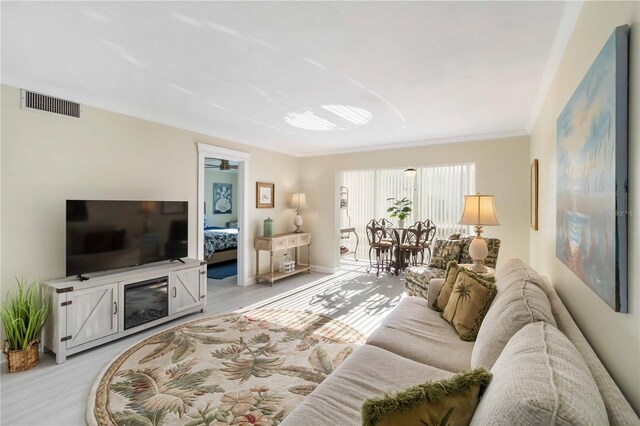 living area with crown molding, light wood finished floors, baseboards, and visible vents