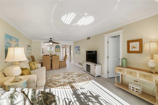 living room with baseboards, crown molding, visible vents, light wood-style floors, and ceiling fan