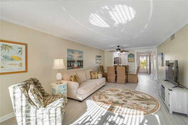 living room featuring light wood finished floors, baseboards, ornamental molding, and visible vents