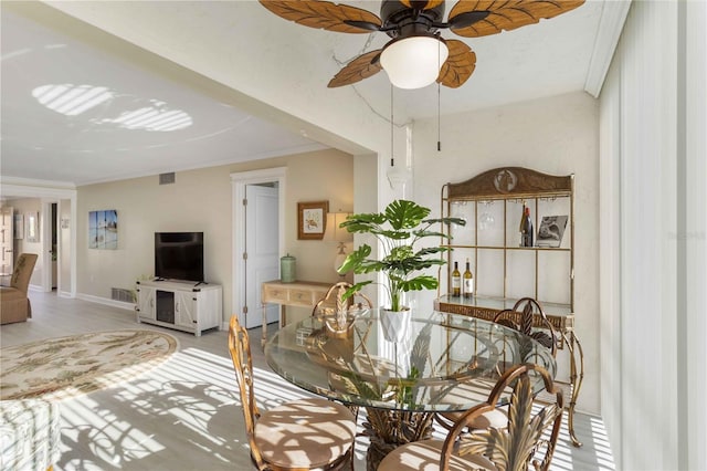 dining area featuring light wood-type flooring, baseboards, crown molding, visible vents, and ceiling fan