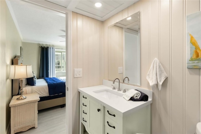 bathroom featuring vanity, ensuite bath, crown molding, a decorative wall, and wood finished floors