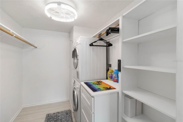 laundry area with baseboards, stacked washer and clothes dryer, a textured ceiling, laundry area, and light wood finished floors
