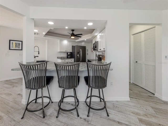 1232 Pine Needle Rd, Venice, FL 34285 - kitchen with a tray ceiling, a peninsula, white cabinetry, a sink, and stainless steel appliances