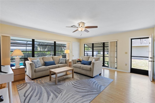 living room featuring light wood-style flooring, baseboards, and a ceiling fan