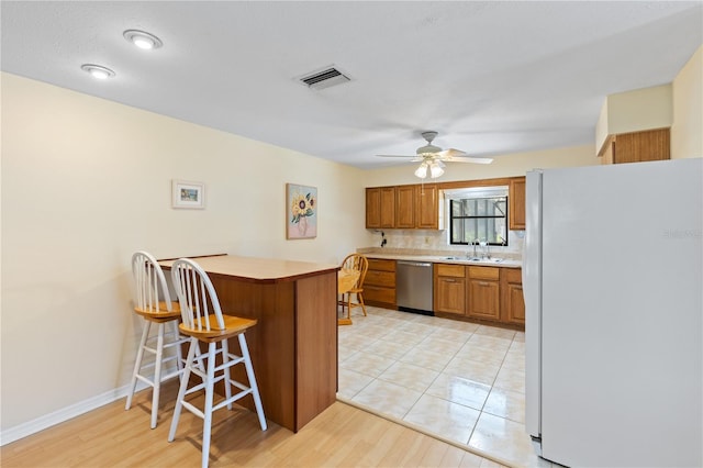 kitchen featuring freestanding refrigerator, stainless steel dishwasher, visible vents, a sink, and brown cabinets
