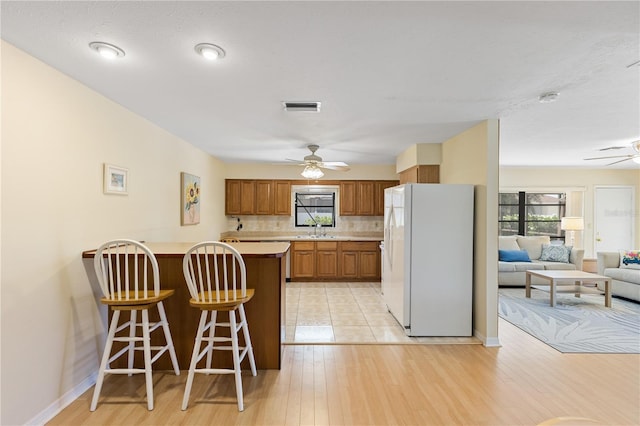kitchen featuring ceiling fan, white fridge with ice dispenser, a peninsula, visible vents, and a sink