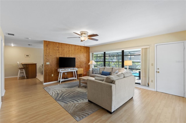 living area with visible vents, baseboards, ceiling fan, light wood-style floors, and wooden walls