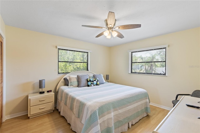 bedroom with baseboards, multiple windows, ceiling fan, and light wood-style floors