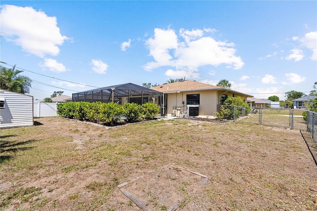 rear view of house with stucco siding, a fenced backyard, a lanai, a yard, and a gate